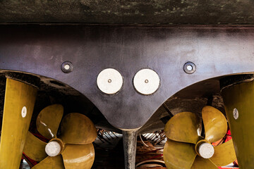 The back of a large motor yacht, standing on wooden blocks in a dry dock. Two propellers and zinc protective inserts. - obrazy, fototapety, plakaty