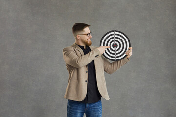 Happy smiling young man holding a shooting target and pointing right at the center at the bullseye...
