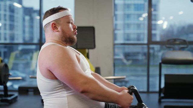 Fat burning, overweight man lifting blocks on rowing machine, training on block device and gym equipment.