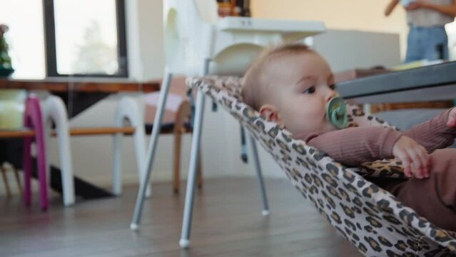 Baby swinging in a crib while mother prepares food