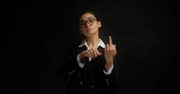Confident, serious business woman in glasses and office clothes shows the middle finger, fuck you, fuck off, with a haughty face. Isolated on a black background in the studio