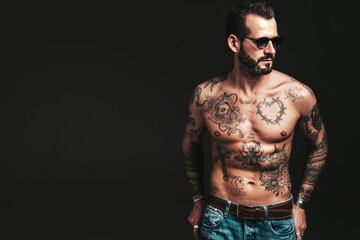 Fototapeta premium Portrait of handsome confident stylish hipster lambersexual model. Sexy modern man. Naked torso with tattoos.Fashion male posing in studio on dark background in sunglasses