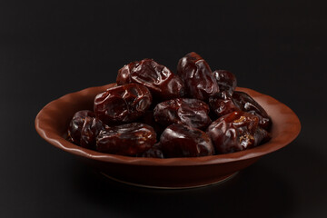 Dates fruit on a plate with black background.