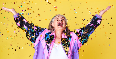 Fototapeta na wymiar Celebrate and enjoy life while you can. Cropped shot of a cheerful and stylish senior woman celebrating with confetti falling over her against a yellow background.