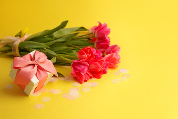 Pink red tulips bouquet, wrapped with ribbon and gift box overbright yellow background. Copy space. Happy Easter, 8 march, Woman day, Saint Valentine, Birthday, Mom day, banner