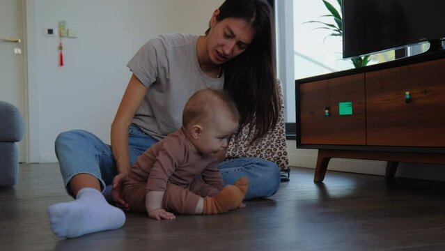 Young mom sitting with baby on apartment floor playing