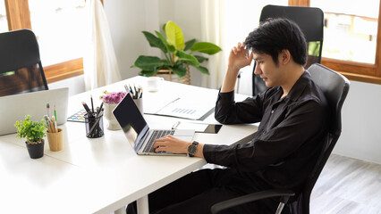 Serious and stressed Asian businessman analyses some data on laptop