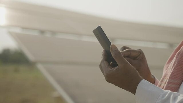 Handheld Close Up Shot Of Farmer Hand Using Smartphone Infront Of Solar Panel At Farmland With Copy Space - Concept Of Renewable Energy, Modern Agriculture And Technology.