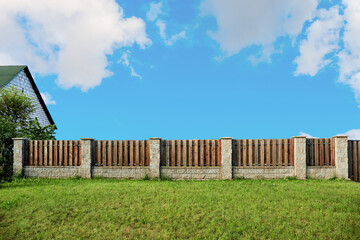 Fototapeta premium Brown wooden plank fence with block posts. House wall. Green grass lawn. Countryside private property. Minimalist landscape design. Rural real estate. Neighbors. Isolated mockup design. Exterior