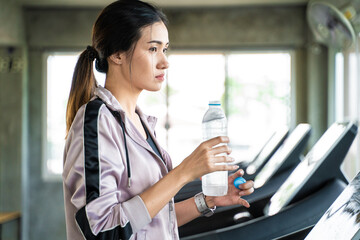 Asian sport women drinking water from bottle after running in fitness gym