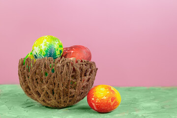 Colored eggs in nest on green and pink background. Easter. Copy space