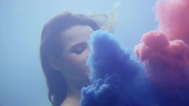 dream and fantasy, young woman is swimming underwater, clouds of blue and pink paints are swaying