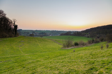 Obraz premium A sunset during spring over het rolling hill landscape in the south of the Netherlands with a view on the small village Slenaken, the meadows and in the background the sun going down