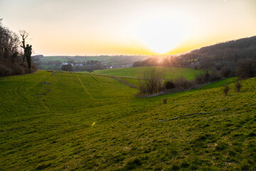 A sunset during spring over het rolling hill landscape in the south of the Netherlands with a view on the small village Slenaken, the meadows and in the background the sun going down