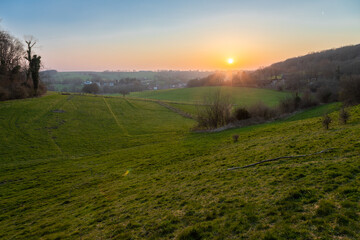 A sunset during spring over het rolling hill landscape in the south of the Netherlands with a view on the small village Slenaken, the meadows and in the background the sun going down