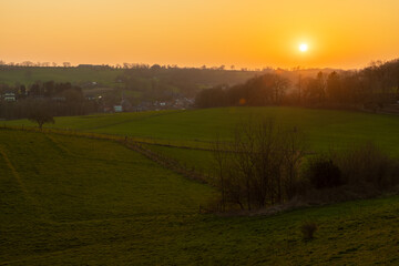 A sunset during spring over het rolling hill landscape in the south of the Netherlands with a view on the small village Slenaken, the meadows and in the background the sun going down