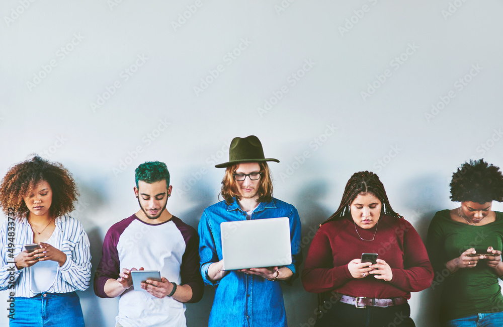 Aufkleber consumed with media. studio shot of a group of young people standing against a wall and using wirele