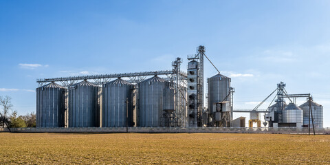 Obraz premium panorama view on agro silos granary elevator on agro-processing manufacturing plant for processing drying cleaning and storage of agricultural products, flour, cereals and grain.