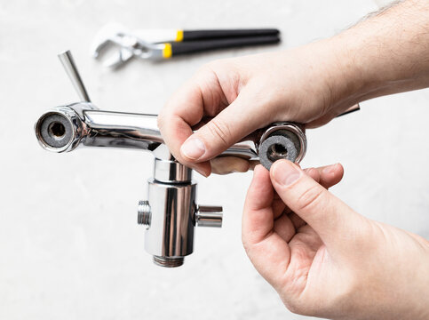 top view of plumber hands install paronite gasket in shower faucet and adjustable wrench on concrete board in background