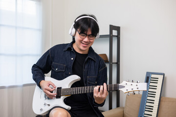 Lifestyle concept. Young asian musician playing electric guitar in living room at home on this weekend. Relaxing with song and music. Asian man having fun playing rock guitar