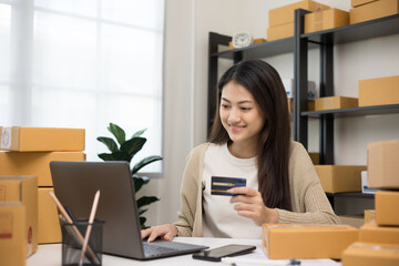 Shopping online. Young asian woman input the serial number of credit card to laptop for shopping payment. Buy item online delivery at home. Small business entrepreneur with many parcel box on table