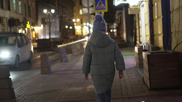 a little girl in a blue jacket and hat walks alone down a night street, turns around and is frightened. helping children in difficult situations. street children. escapes of teenagers from home.