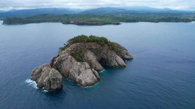 Aerial view circling the Ilheu de Santana islet, on the coast of cloudy Sao Tome