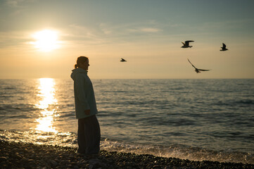 Caucasian woman feeding seagulls at sunset by the sea. 