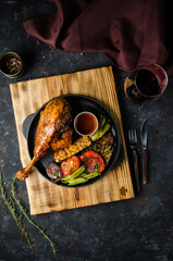 great fresh baked turkey leg and sliced piece sprinkled with spices lying on a blue plate to black wooden background