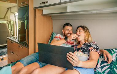 Young man feeding his girlfriend a popcorn while they watch a movie on the tablet lying on the bed...