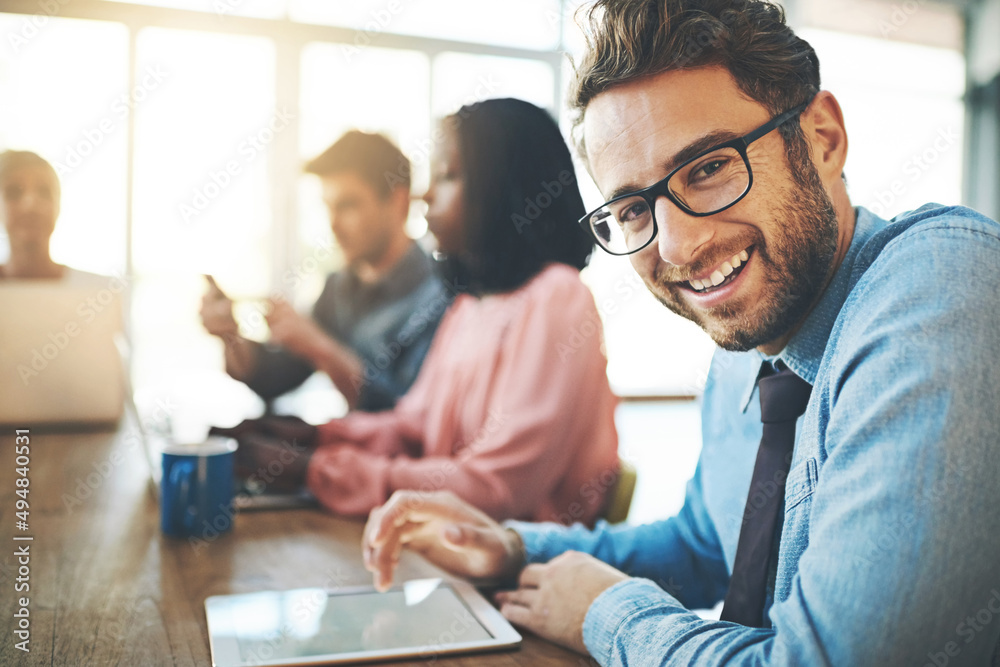 Aufkleber Feeling optimistic about the future of his career. Portrait of a businessman using a digital tablet with his colleagues in the background.