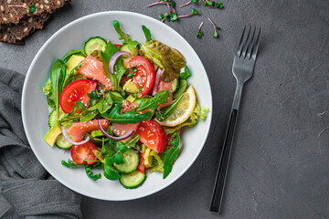 Salad with salmon, avocado, cucumber and tomatoes on a dark gray background.