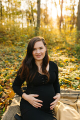 Beautiful pregnant woman in a black dress in the autumn park. Golden autumn. Fallen leaves. Awaiting the birth of a child.