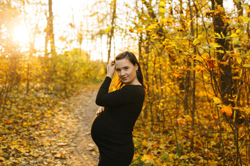 Beautiful pregnant woman in a black dress in the autumn park. Golden autumn. Fallen leaves. Awaiting the birth of a child.