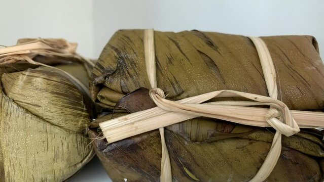 4K Time Lapse Thai traditional sweet banana wrapped with sticky rice by banana leaf defrosting on a white background. Strings made of shredded banana stems from banana tree. In Thai is "Khao Tom Mad"