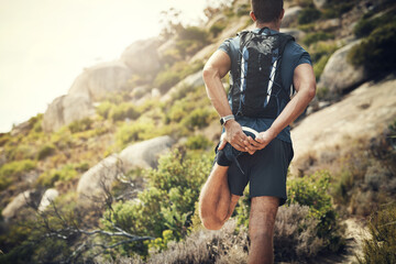 Warming up while taking in the view. Rearview shot of an unrecognizable young man stretching before heading off on his hike in the mountains.