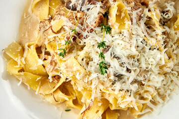 Tagliatelle pasta with mushrooms and sauce, parmesan in a white plate. Close-up