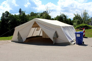 Outside view of white field hospital tent built by military on paved parking lot and used for COVID-19 coronavirus outdoor testing next to plastic blue garbage container used for medical waste