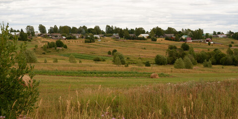 Fototapeta na wymiar Beautiful rustic summer landscape with old wooden houses and hay in the field