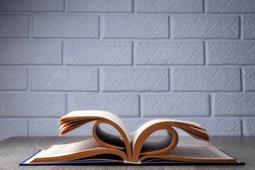 An open book on the table against the background of a wall of white decorative bricks. Education and Information