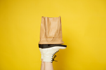 White women's shoes hold a beige bag on a yellow isolated background. Fashionable idea for...