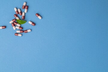Colored capsules with medical drugs and a green leaf on a blue background. Copy space, flat lay