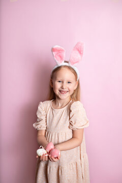 Happy Easter. A cute girl with rabbit ears holds colored eggs in her hands and smiles cheerfully. pink background. Space for text.