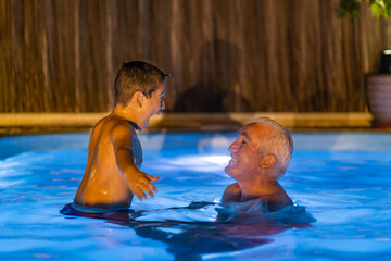 Grandfather and grandson  playing in a swimming pool at night