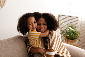 Younger and older sister spending time together at home. Two black girls of different age messing...
