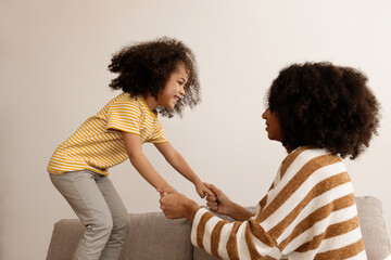 Younger and older sister spending time together at home. Two black girls of different age messing...