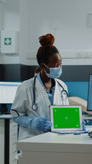 Patient and medic looking at horizontal green screen on tablet and wearing face masks for protection. Woman and doctor doing checkup with chroma key and isolated mockup template.