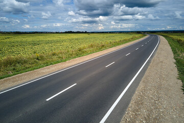 Aerial view of empty intercity road between green agricultural fields. Top view from drone of highway roadway
