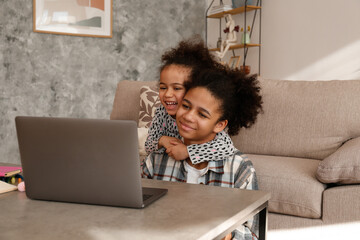 Two beautiful black girls of different age on a video call at home. Loving sisters sitting together by the table with laptop. Interior background, close up, copy space.