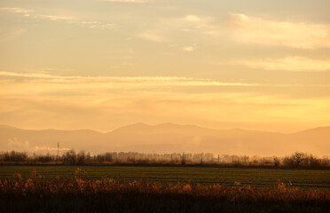 Beautiful evening panoramic landscape with bright setting sun over distant mountain peaks and asphalt road in front at sunset